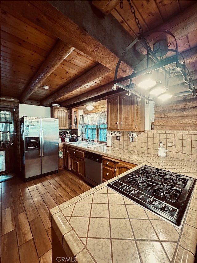 kitchen with appliances with stainless steel finishes, kitchen peninsula, beam ceiling, light hardwood / wood-style flooring, and tile counters