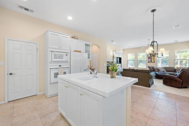 kitchen featuring white appliances, white cabinets, open floor plan, light countertops, and a sink