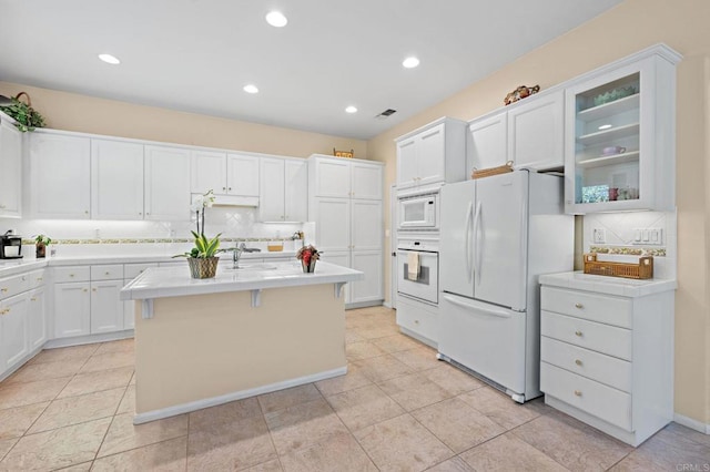 kitchen featuring light countertops, glass insert cabinets, white cabinetry, an island with sink, and white appliances