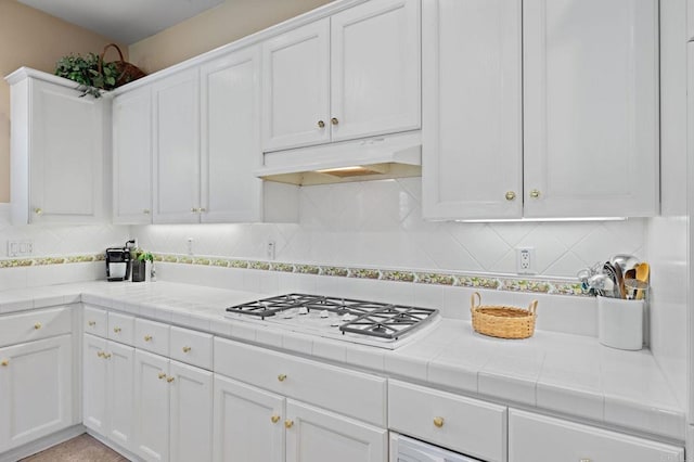 kitchen featuring tile countertops, white gas stovetop, backsplash, white cabinetry, and under cabinet range hood