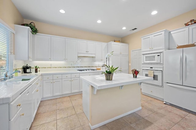 kitchen with white appliances, a kitchen island, visible vents, and white cabinets