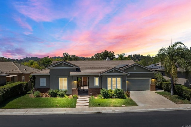 ranch-style home with a tile roof, brick siding, concrete driveway, a lawn, and an attached garage