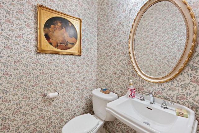 bathroom with a sink, toilet, and wallpapered walls