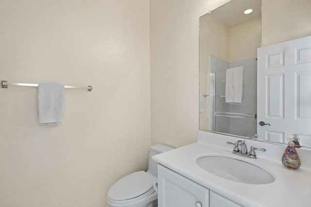 bathroom featuring a shower with door, vanity, and toilet