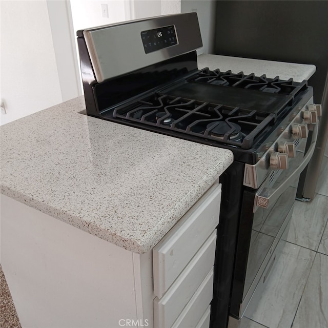 kitchen featuring light stone countertops, white cabinetry, and gas stove