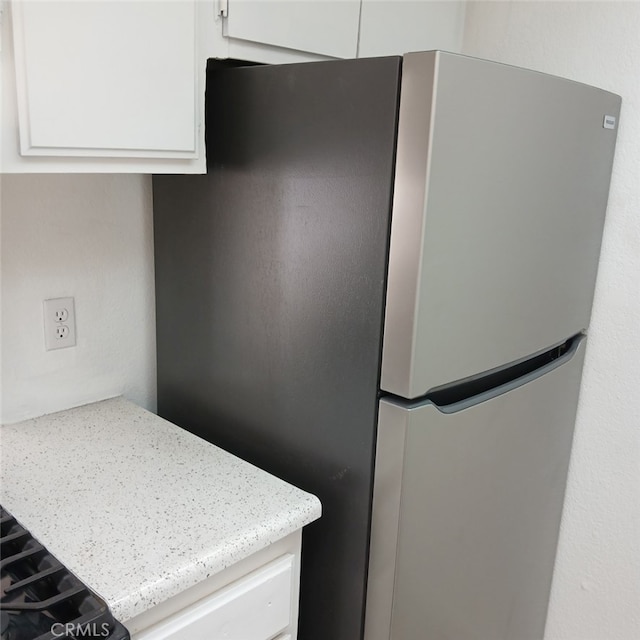 kitchen with light stone countertops, stainless steel fridge, and white cabinets