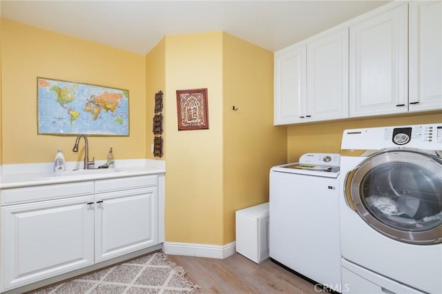 clothes washing area featuring cabinets, light hardwood / wood-style flooring, washer and dryer, and sink