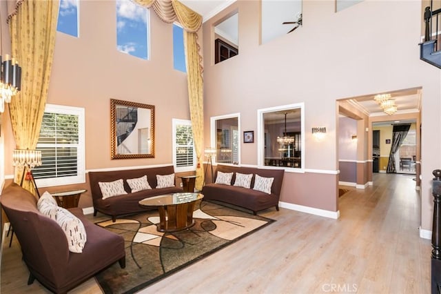 living room with a towering ceiling, light hardwood / wood-style floors, ceiling fan with notable chandelier, and ornamental molding