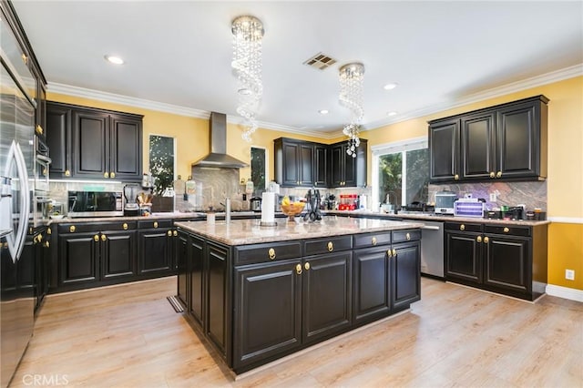 kitchen with light stone countertops, a center island, stainless steel appliances, wall chimney range hood, and light hardwood / wood-style floors