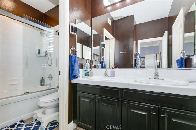 full bathroom featuring combined bath / shower with glass door, vanity, and toilet