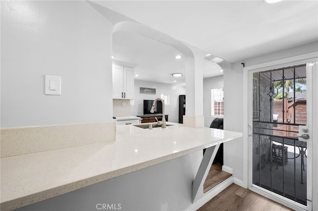 kitchen with light stone countertops, sink, white cabinets, and light hardwood / wood-style floors