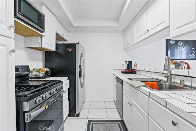 kitchen with white cabinets, a raised ceiling, sink, appliances with stainless steel finishes, and tile counters