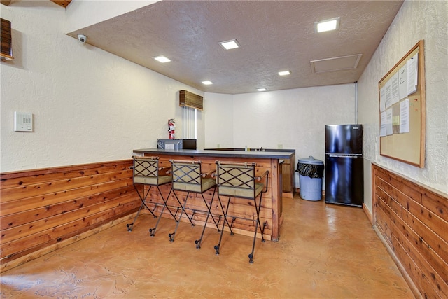 bar featuring wood walls, black refrigerator, and a textured ceiling