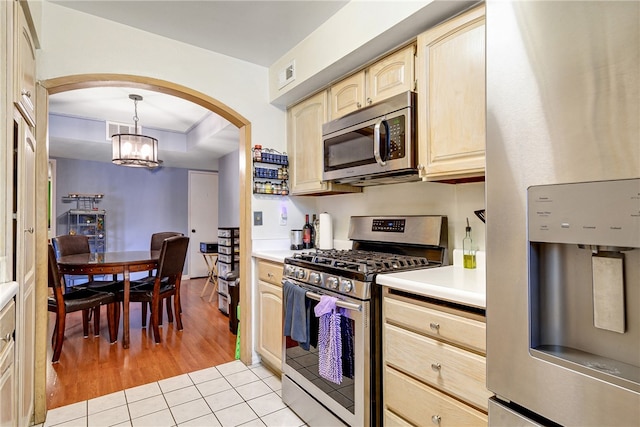 kitchen with an inviting chandelier, light wood-type flooring, pendant lighting, light brown cabinetry, and appliances with stainless steel finishes