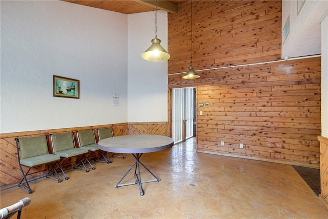 dining space featuring wooden walls, a towering ceiling, and concrete flooring