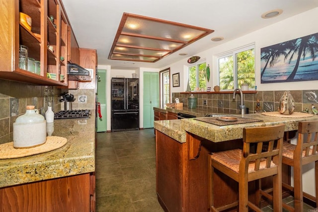 kitchen with tasteful backsplash, kitchen peninsula, black fridge, and sink