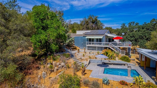 rear view of property featuring a pool with hot tub, solar panels, and a patio