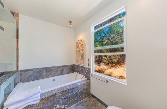 bathroom with tiled bath and a healthy amount of sunlight