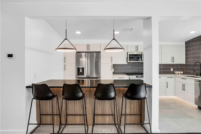 kitchen featuring stainless steel appliances, a breakfast bar, sink, and decorative light fixtures