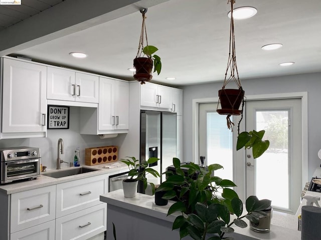 kitchen featuring stainless steel fridge, white cabinets, decorative light fixtures, and sink