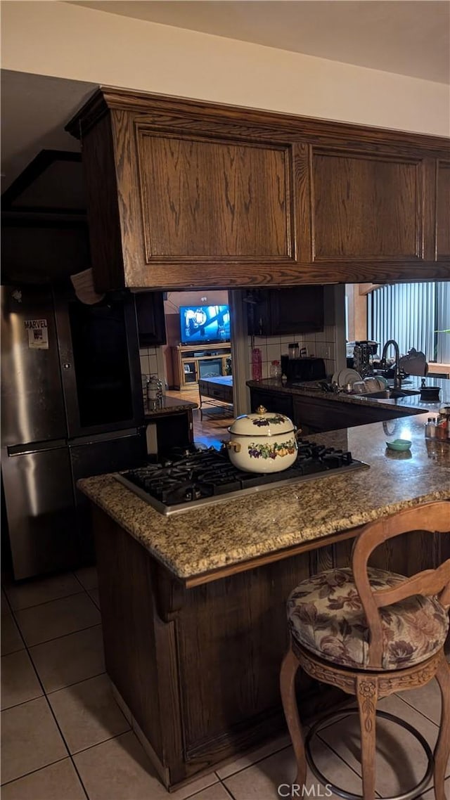 kitchen with stone counters, black fridge, dark brown cabinetry, and light tile patterned floors