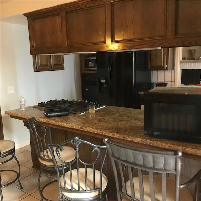 kitchen with decorative backsplash, light tile patterned floors, dark stone countertops, and black appliances