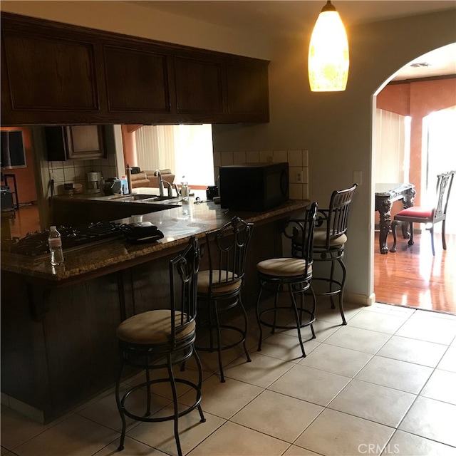 bar with decorative backsplash, dark stone countertops, light tile patterned floors, and a wealth of natural light