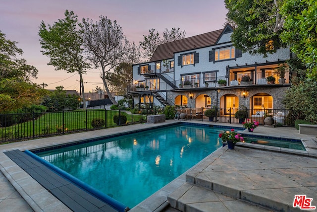 pool at dusk with a patio area and an in ground hot tub