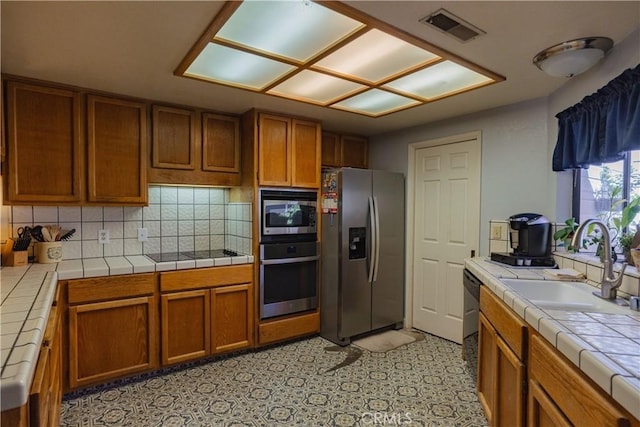 kitchen with tile countertops, sink, appliances with stainless steel finishes, and tasteful backsplash