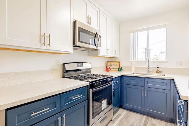 kitchen featuring sink, blue cabinets, appliances with stainless steel finishes, white cabinets, and light wood-type flooring