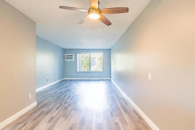 empty room featuring ceiling fan, an AC wall unit, a textured ceiling, and light hardwood / wood-style flooring