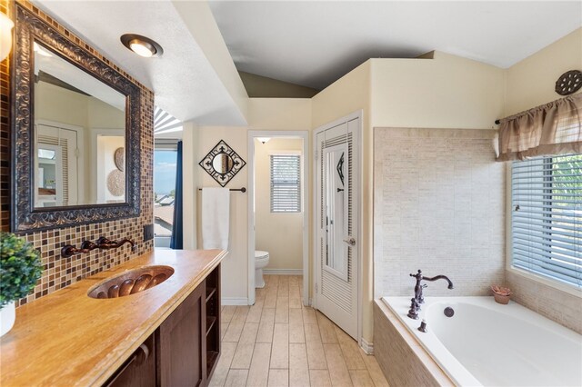 bathroom featuring tiled bath, hardwood / wood-style floors, vanity, and toilet