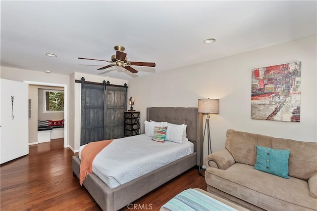 bedroom with ceiling fan, dark hardwood / wood-style flooring, and a barn door