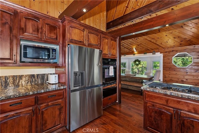 kitchen with dark stone countertops, beam ceiling, wooden walls, dark wood-type flooring, and stainless steel appliances