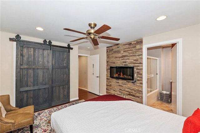 bedroom with ceiling fan, ensuite bath, a barn door, and a fireplace