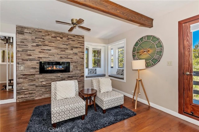 sitting room featuring ceiling fan, dark hardwood / wood-style flooring, a tiled fireplace, and beamed ceiling