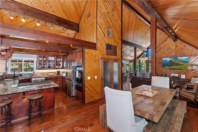 dining room with beam ceiling, rail lighting, wood walls, and dark wood-type flooring