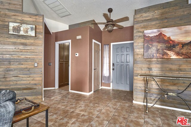 foyer with a textured ceiling, lofted ceiling, wood walls, and ceiling fan