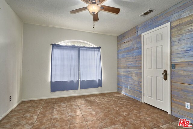 unfurnished room with a textured ceiling, wood walls, and ceiling fan