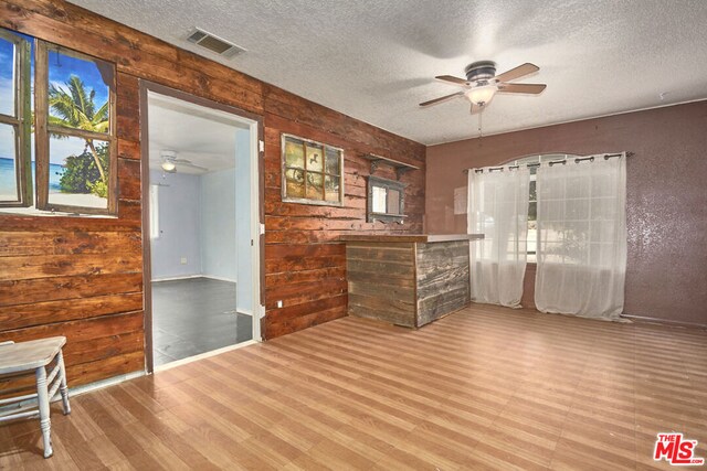 spare room featuring ceiling fan, hardwood / wood-style flooring, wooden walls, and a textured ceiling