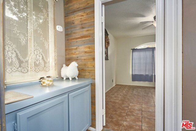 bathroom featuring a textured ceiling, wooden walls, ceiling fan, and tile patterned floors