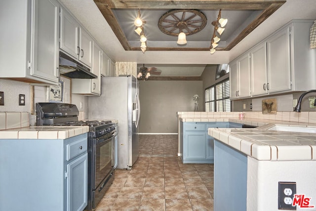 kitchen with black range with gas stovetop, a raised ceiling, kitchen peninsula, light tile patterned floors, and tile counters