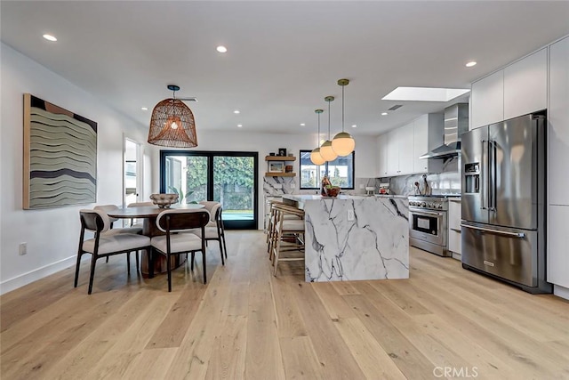 kitchen with a kitchen island, wall chimney exhaust hood, high quality appliances, and decorative light fixtures