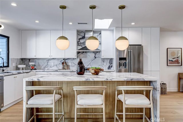 kitchen with white cabinetry, high end fridge, decorative light fixtures, a kitchen island, and light stone counters