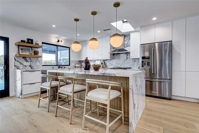 kitchen featuring light stone countertops, pendant lighting, white cabinets, a kitchen island, and high end fridge