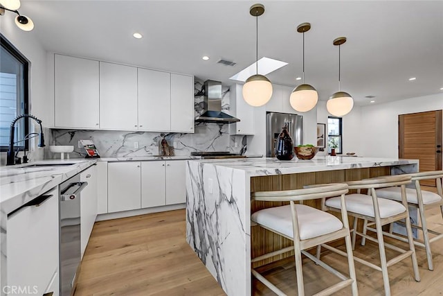 kitchen featuring stainless steel appliances, decorative light fixtures, light stone countertops, a kitchen island, and wall chimney range hood