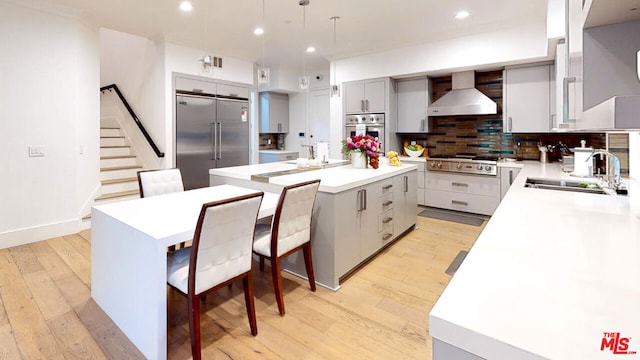 kitchen featuring light hardwood / wood-style flooring, wall chimney exhaust hood, stainless steel appliances, and a center island