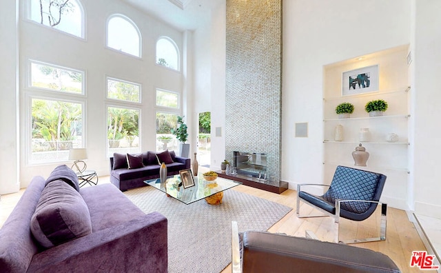 living room with light wood-type flooring, a towering ceiling, and plenty of natural light