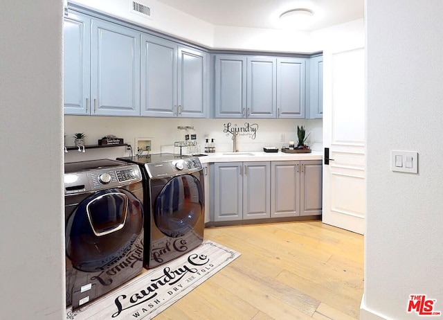 laundry area featuring washer and clothes dryer, light hardwood / wood-style flooring, and cabinets