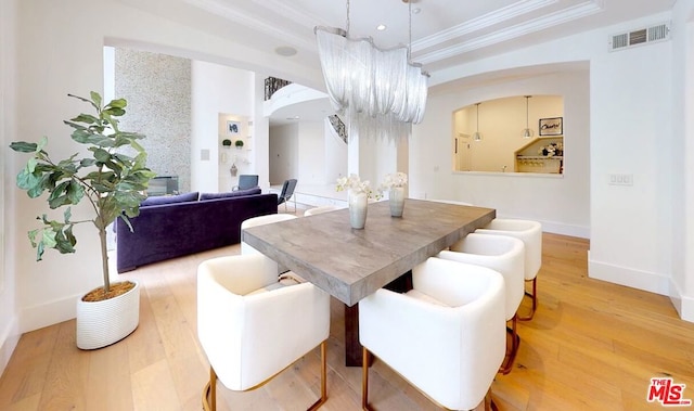 dining space with an inviting chandelier, a raised ceiling, crown molding, and hardwood / wood-style floors